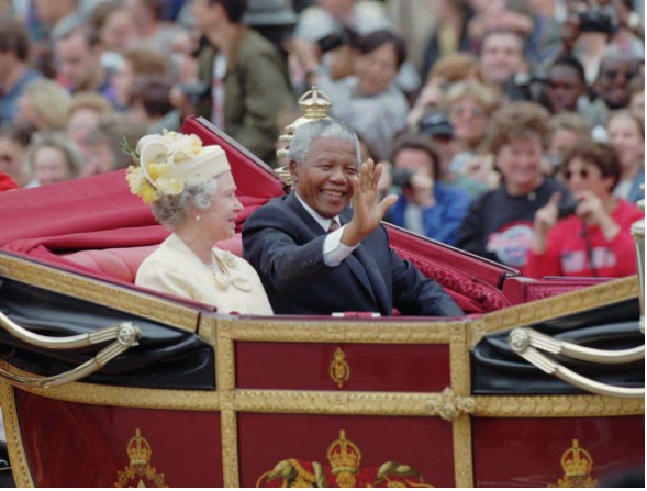 South African President Nelson Mandela waves to crowds as he sits next to Queen Elizabeth II in an open carriage on the way to Buckingham Palace in London